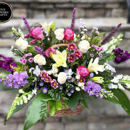 Large mixed basket arrangement with pink and white roses, lilies, and purple accent flowers.