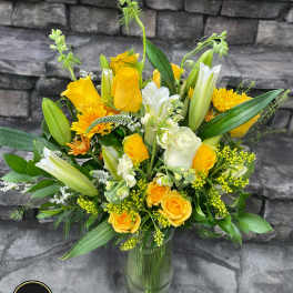 Tall yellow and white arrangement with roses and lilies in a clear glass vase