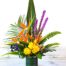 Tropical arrangement with yellow roses and orange bird-of-paradise in a glass vase
