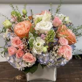 Pastel bouquet of roses, hydrangeas, and white blooms in a square vase