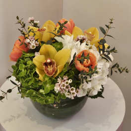 Mixed bouquet of yellow and orange flowers in a dark bowl vase