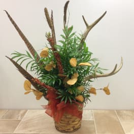 Tall arrangement of greenery with dried seed heads and antler-like branches in a woven basket