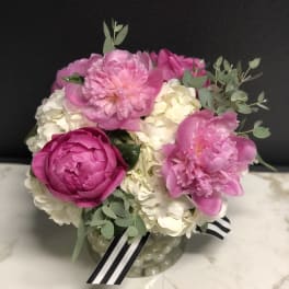 Pink peonies and white hydrangeas in a glass vase with a striped ribbon