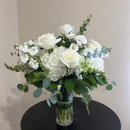 White roses and hydrangeas with eucalyptus in a clear glass vase on a round black table