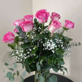 Tall arrangement of pink roses with baby's breath in a clear glass vase.