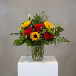 Bouquet of red roses and yellow sunflowers in a clear glass vase