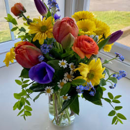 Colorful mixed bouquet in a clear glass vase with tulips, daisies, and ranunculus