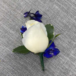 White rose boutonniere with blue accent flowers on gray fabric