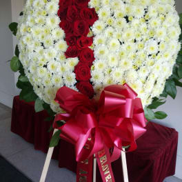 Heart-shaped floral tribute of white chrysanthemums and red roses with a large red bow