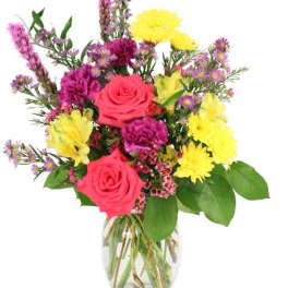 Mixed bouquet of pink roses, yellow daisies, and purple flowers in a glass vase