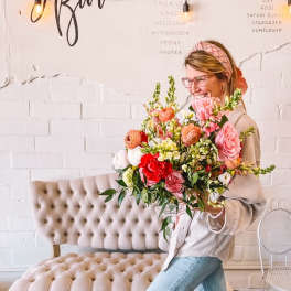 Woman holding a large mixed bouquet of pink, red, white, and peach flowers
