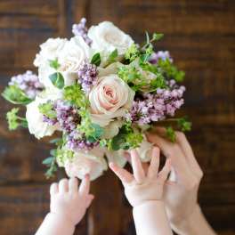 Handheld bouquet of pale pink and white roses with lilac flowers