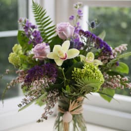 Bouquet of orchids, roses, and purple filler flowers in a glass vase