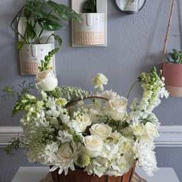 White floral arrangement in a wooden basket with roses and daisies