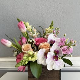 Mixed bouquet in a wooden box with pink tulips, roses, and white orchids