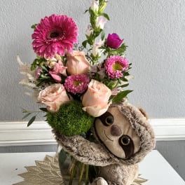 Pink flower arrangement with a plush sloth in a glass vase