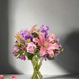 Pink lilies and roses with purple flowers in a clear glass vase