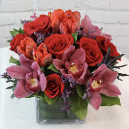 Bouquet of red roses and pink orchids in a square glass vase