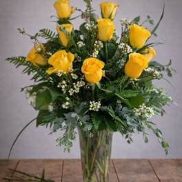 Yellow roses arranged in a clear glass vase with greenery