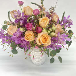 Mixed bouquet of peach roses and purple orchids in a white vase