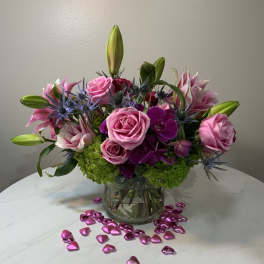 Pink roses and lilies arranged in a glass vase with heart confetti