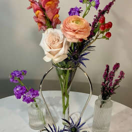 Mixed flowers arranged in a clear vase with small accent vases on a table