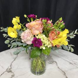 Mixed bouquet of pink, yellow, and peach flowers in a glass vase