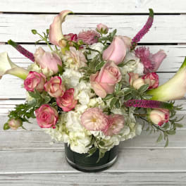 Low pink and white bouquet with roses, calla lilies, and hydrangeas in a glass cylinder vase