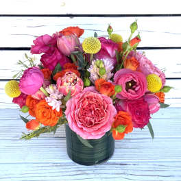 Bright arrangement of pink and orange roses, ranunculus, and tulips in a green glass vase