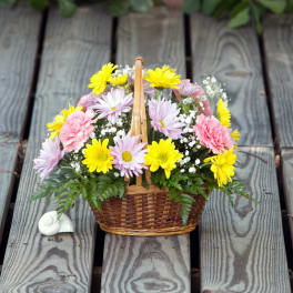 Basket of yellow, pink, and lavender flowers on a wooden deck
