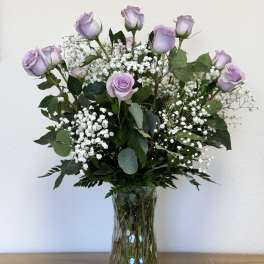 Lavender roses arranged in a clear glass vase with white baby's breath