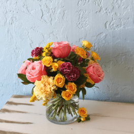 Mixed bouquet of pink, yellow, and burgundy flowers in a clear glass vase