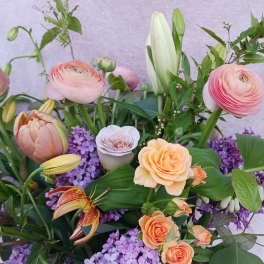 Garden-style arrangement with peach roses, pink ranunculus, lilies, and purple lilacs