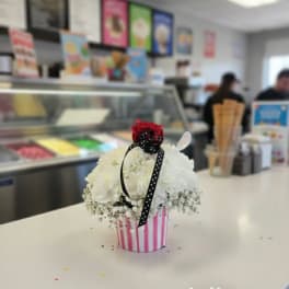 White floral arrangement in a pink striped container with a red rose topper