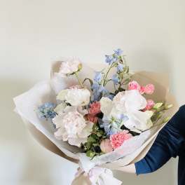 Hand-tied bouquet of pastel pink, white, and blue flowers wrapped in paper