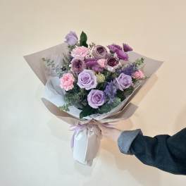 Hand-tied bouquet of lavender roses and pink flowers wrapped in paper