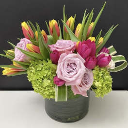 Low glass vase arrangement of pink roses, tulips, and green hydrangeas.