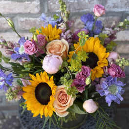 Mixed bouquet with sunflowers, peach roses, and purple blooms in a vase