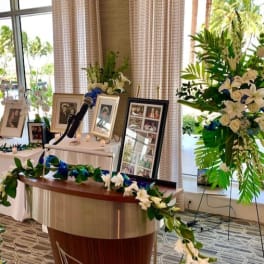 White floral funeral display with framed photos and a microphone stand
