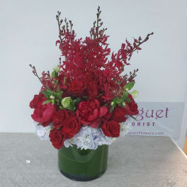 Red roses and orchids arranged in a green glass vase