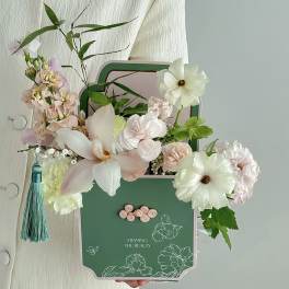 Pastel floral arrangement in a green decorative box with a tassel