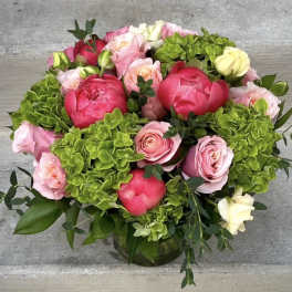 Round arrangement of pink roses, coral peonies, and green hydrangeas in a glass vase