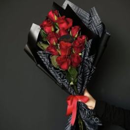 Handheld bouquet of red roses wrapped in black paper with a red ribbon