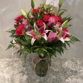 Pink roses and lilies arranged in a glass vase with a ribbon