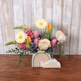 Short pastel flower arrangement in a rainbow-shaped ceramic container