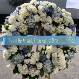 Large white and blue funeral wreath on an easel with a memorial ribbon