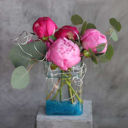 Pink peonies in a clear glass vase with eucalyptus and wire accents