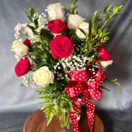 Bouquet of red and white roses with baby's breath and a red polka-dot ribbon in a glass vase
