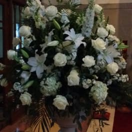 Tall white floral arrangement with roses, lilies, and hydrangeas in a stone urn
