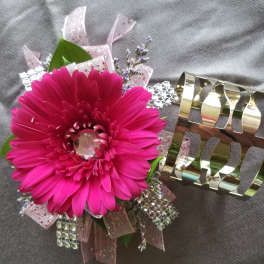 Pink gerbera daisy wrist corsage with rhinestones and gold cuff bracelet on gray fabric